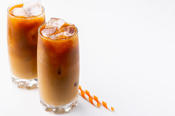 Ice coffee in a tall glass with cream poured over and coffee beans. Cold summer drink on white...