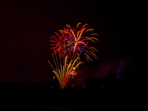 Beautiful vibrant and colorful red and orange floral shaped fourth of July independence day celebratory fireworks exploding in the black night sky.