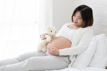 Pregnant women with teddy bear on white bed