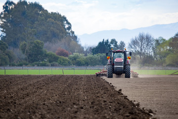 A farmer ploughs a field on a farm using a red tractor and plough