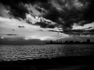 Beautiful black and white photograph of the Chicago skyline at sunset with the water of Lake Michigan below and fluffy clouds in the sky above.
