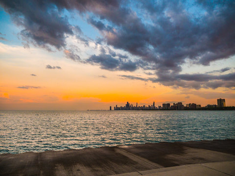 Gorgeous blue and orange colored sunset over the skyline of Chicago with the water of Lake Michigan Below and fluffy clouds in the sky above from Montrose Beach.