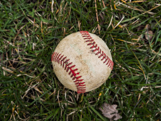 Close up sports background image of an old used weathered leather baseball ball laying in the grass field outside showing intricate detailing and red laces.