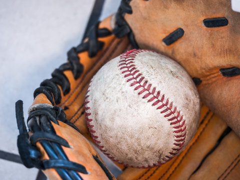 Close up sports background image of an old used weathered leather baseball with red laces inside of a baseball glove or mitt showing intricate detailing and black leather lacing.