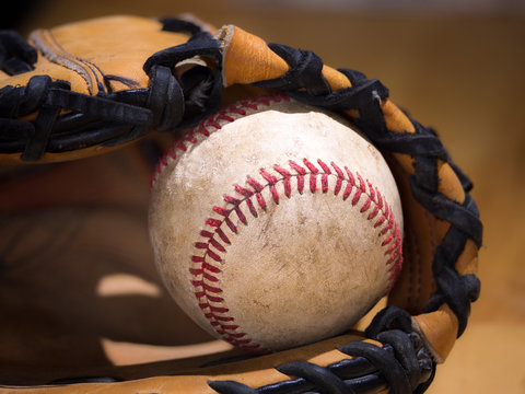 Close up sports background image of an old used weathered leather baseball with red laces inside of a baseball glove or mitt showing intricate detailing and black leather lacing.