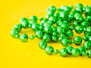 Closeup photograph of a pile of disco ball shaped beads from a plastic green necklace laying on a bright saturated yellow background creating a beautiful juxtaposed colorful background image.