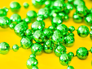 Closeup photograph of a pile of disco ball shaped beads from a plastic green necklace laying on a bright saturated yellow background creating a beautiful juxtaposed colorful background image.