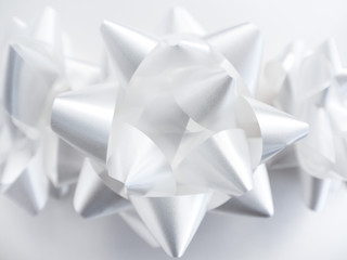 Close-up photograph of three manufactured shiny and pointy white ribbon bows centered and isolated on a white background making a perfect holiday or celebration background.