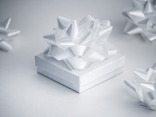 Close-up photograph of a small white glossy gift box with a manufactured shiny white ribbon bow on top isolated on a white background.