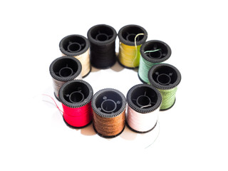 Closeup photograph of several rainbow colored spools of cotton thread or string including red, green, black, yellow, and white organized in a circle and isolated on a white background.