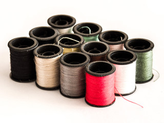 Closeup photograph of several rainbow colored spools of cotton thread or string including red, green, black, yellow, and white organized in rows and isolated on a white background.