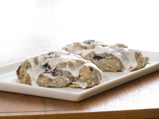 Delicious photograph of a two homemade blueberry scones displayed on a rectangular white serving tray sitting on a dark wood grained table with bright background.