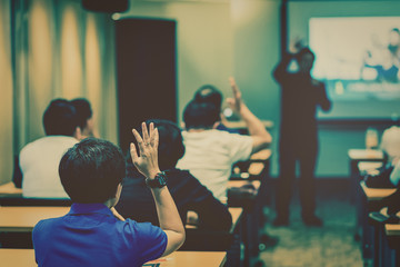 Speaker on the stage in front of the room with Rear view of Audience in put hand up acton for answer the question in the meeting or seminar meeting, business and education concept