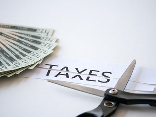 Close up photograph of a scissors cutting a paper that has taxes typed on it with 20 dollar US...