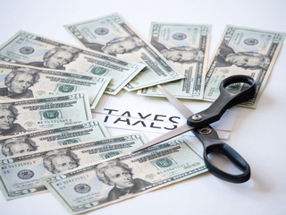 Close up photograph of a scissors cutting a paper that has taxes typed on it with 20 dollar US money representative of government tax cuts and saving money. - obrazy, fototapety, plakaty