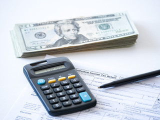 Close-up photograph of a hard copy of an individual income tax return with black calculator and 20 dollar bills piled up representative of United States federal tax cuts and savings this year.