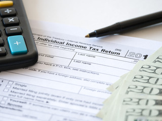 Fototapeta premium Close-up photograph of a hard copy of an individual income tax return with black calculator and 20 dollar bills piled up representative of United States federal tax cuts and savings this year.