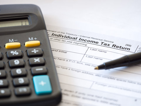 Close up photograph of individual income federal tax return paperwork with calculator and black ballpoint pen at borders for a nice tax season background, backdrop or wallpaper image.