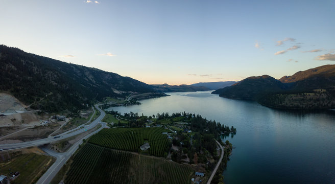 Aerial panoramic view of homes near a lake during a vibrant summer sunset. Located near Kelowna and Vernon, BC, Canada.