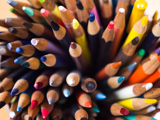Detailed macro photograph view of the tops of a container of many sharpened colored art pencils from above.