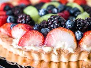 Closeup photograph of a beautiful and colorful vibrant fruit tart dessert with blueberry, strawberry, kiwi and blackberry fruit topping and browned fluted crust edge set on a kitchen counter top.