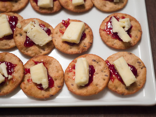 Close up photograph of delicious easy to make homemade appetizer composed of crackers, cheese, and jelly on a white serving plate great for parties such as super bowl or birthday celebrations.