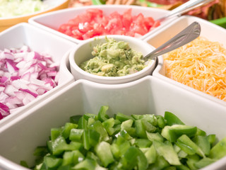 Close up photograph of a white serving tray filled with taco appetizer toppings including cheese, peppers, onion, tomato, guacamole making great background for football party or birthday celebrations.