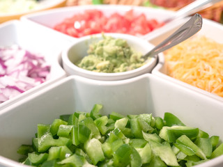 Close up photograph of a white serving tray filled with taco appetizer toppings including cheese, peppers, onion, tomato, guacamole making great background for football party or birthday celebrations.