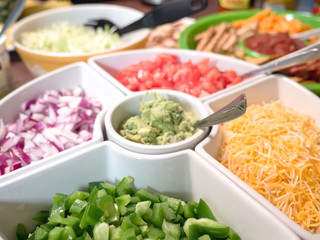 Close up photograph of a white serving tray filled with taco appetizer toppings including cheese, peppers, onion, tomato, guacamole making great background for football party or birthday celebrations.