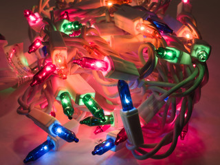 Close up photograph of a pile of colored Christmas lights including green, blue, red, and orange making a festive holiday background.