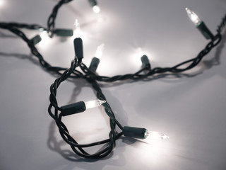 Close-up photograph of real white Christmas string lights with a dark background making a festive...