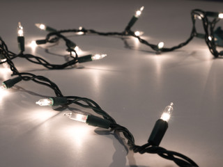 Close-up photograph of real white Christmas string lights with a dark background making a festive holiday backdrop.