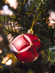 Closeup photograph of a beautiful red glass Christmas ornament hung from an artificial douglas fir green Christmas tree lit with lights for a festive holiday background