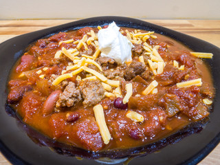Closeup photograph of a black bowl filled with homemade chili with beans, ground beef, tomatoes and topped with cheese and sour cream.