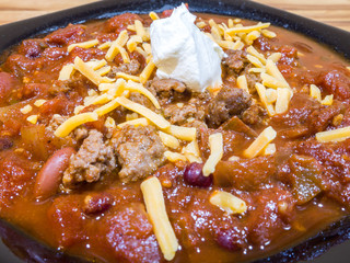 Closeup photograph of a black bowl filled with homemade chili with beans, ground beef, tomatoes and topped with cheese and sour cream.