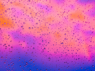 Colorful water droplets on the glass of a window during a rain storm at sunset