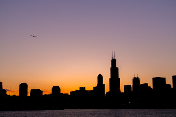 Fototapeta na wymiar Chicago skyline picture during beautiful orange yellow sun as it lowers below the building silhouettes and the water of lake Michigan in the foreground