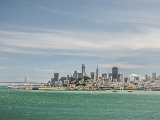 Obraz premium A view of the San Francisco Skyline from across the bay with high rise buildings, bridge and blue feathery cloud sky above.