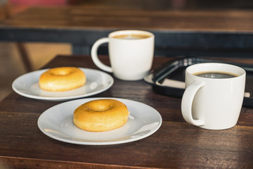 Two set of donuts in a white plate with coffee cups on wooden table