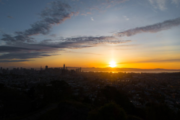 Sunrise over the city of Sanfrancisco and adjacent bay with bright yellow and orange sky from a rocky hill.