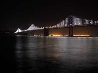 Fototapeta na wymiar Bridge Lights on the San Francisco Oakland Bay bridge at night with water below.