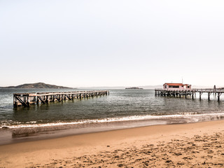 A beautiful seascape or landscape photograph of a two wood Piers extending out into the world famous San Francisco Bay with waves rolling into sandy beach in the foreground and clear sunny sky above.
