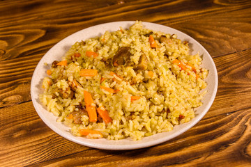 Ceramic plate with pilaf on wooden table