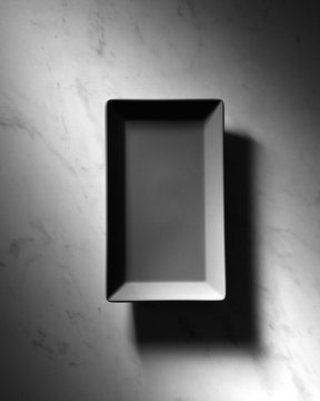 Black rectangular empty plate presented on a gray marble background with shadows, space for text. Top view