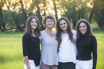 Outdoor Portrait of a beautiful family, a mother and her daughters. Horizontal portrait of beautiful hispanic women standing together in a grass field with the sun at their backs