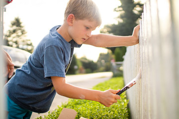 boy painting a white picket fence in the summer