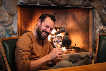 a smiling man enjoying a glass of wine by a fireplace in the fall