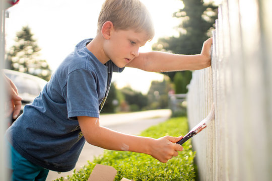 Boy Painting A White Picket Fence In The Summer