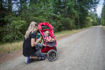 Woman and her little boy taking a break from working out. Playing together and smiling together. Boy riding in a jogging stroller on a scenic running trail