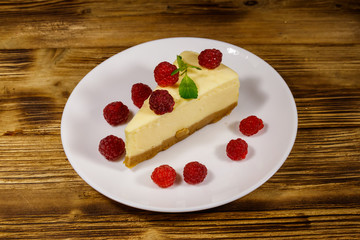 Piece of tasty New York cheesecake with raspberries in a white plate on wooden table